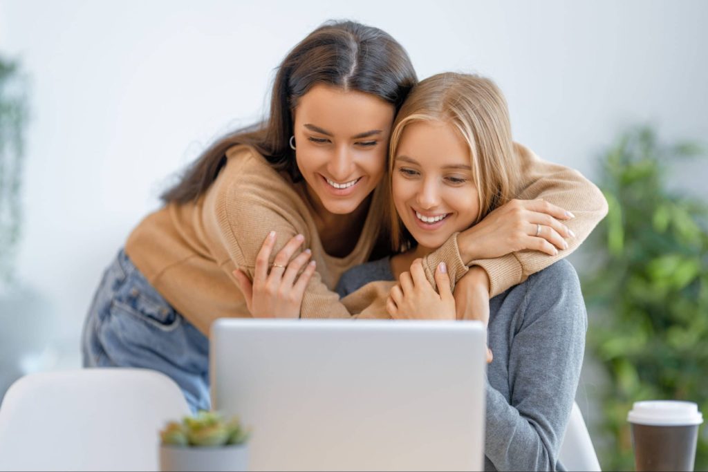 Två unga tjejer kramas framför dator